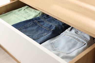 Photo of Chest of drawers with different folded jeans, closeup