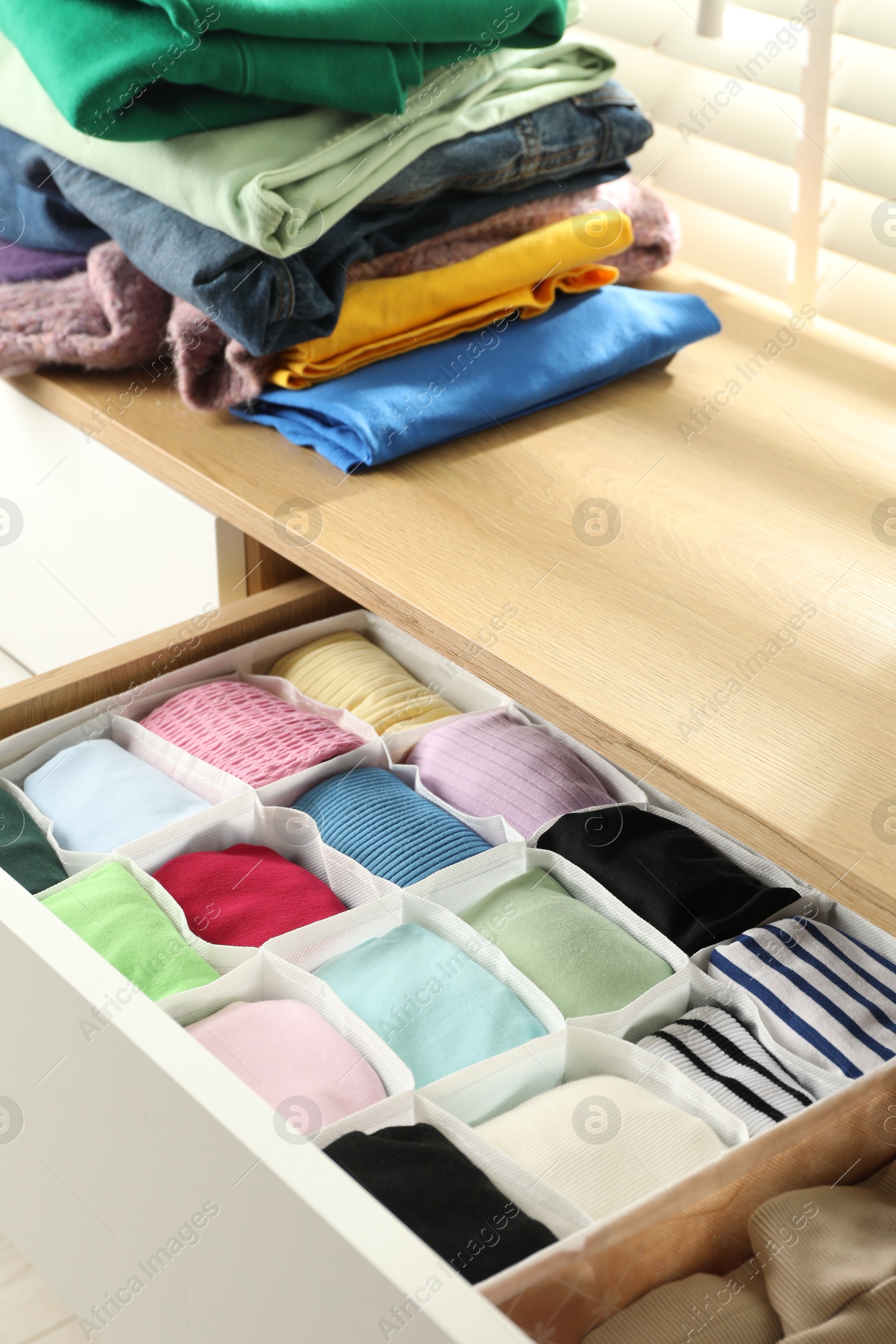 Photo of Chest of drawers with different folded clothes indoors, closeup