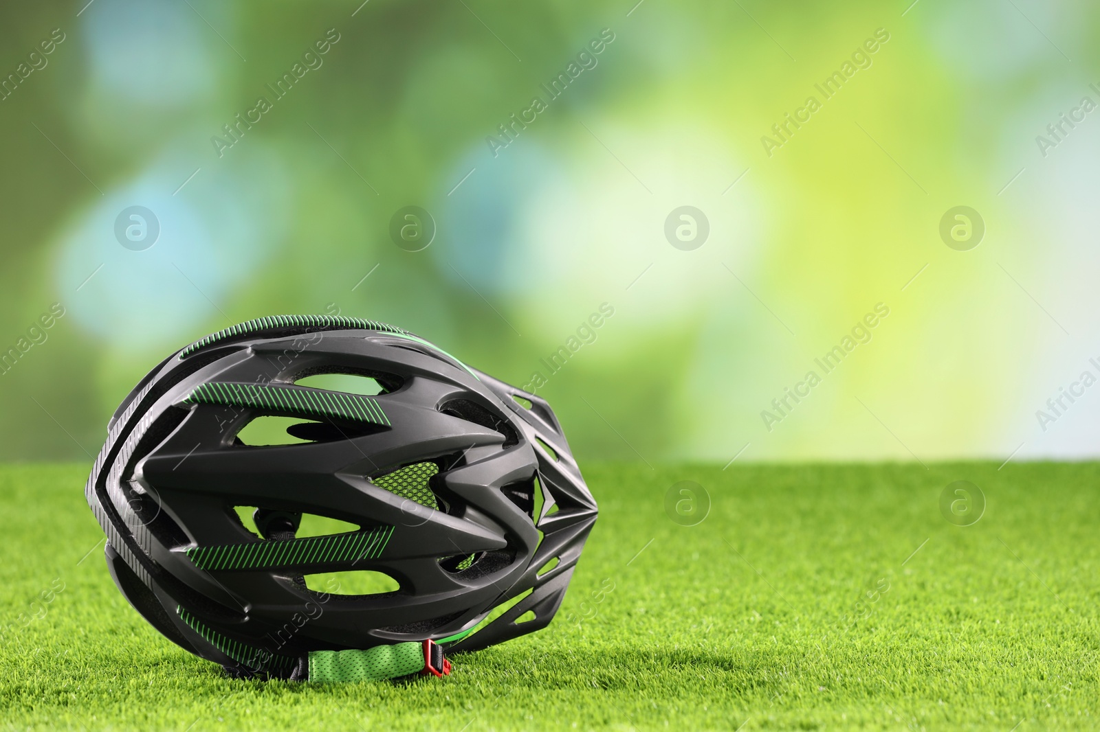 Photo of Stylish protective helmet on green grass against blurred background. Space for text