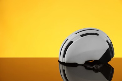 White protective helmet on mirror surface against yellow background. Space for text