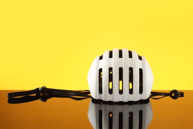 White protective helmet on mirror surface against yellow background. Space for text