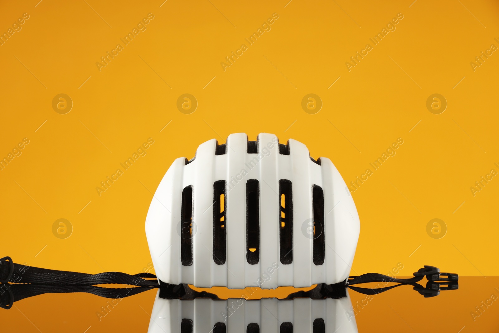 Photo of White protective helmet on mirror surface against orange background