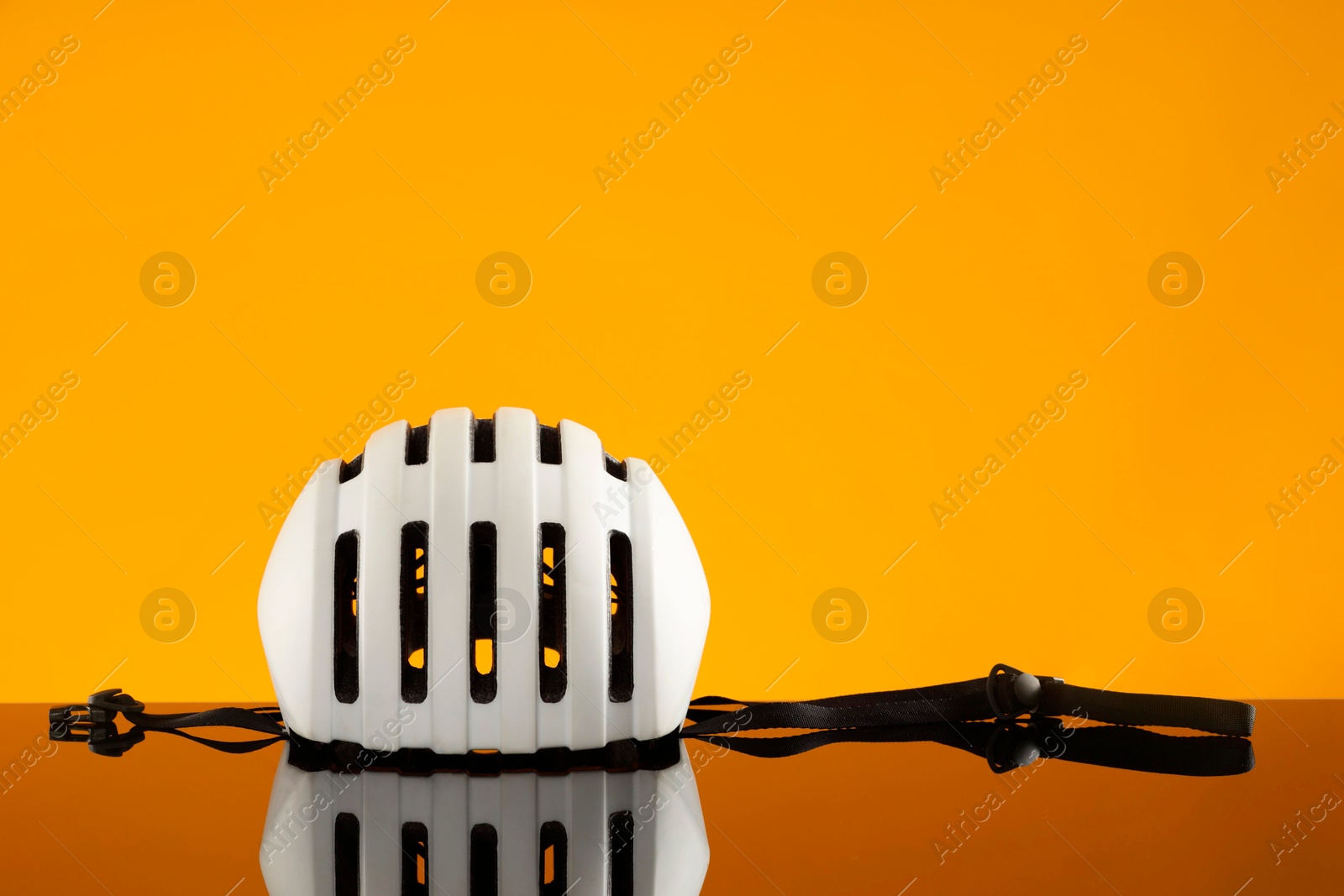 Photo of White protective helmet on mirror surface against orange background. Space for text