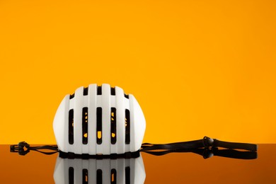 White protective helmet on mirror surface against orange background. Space for text