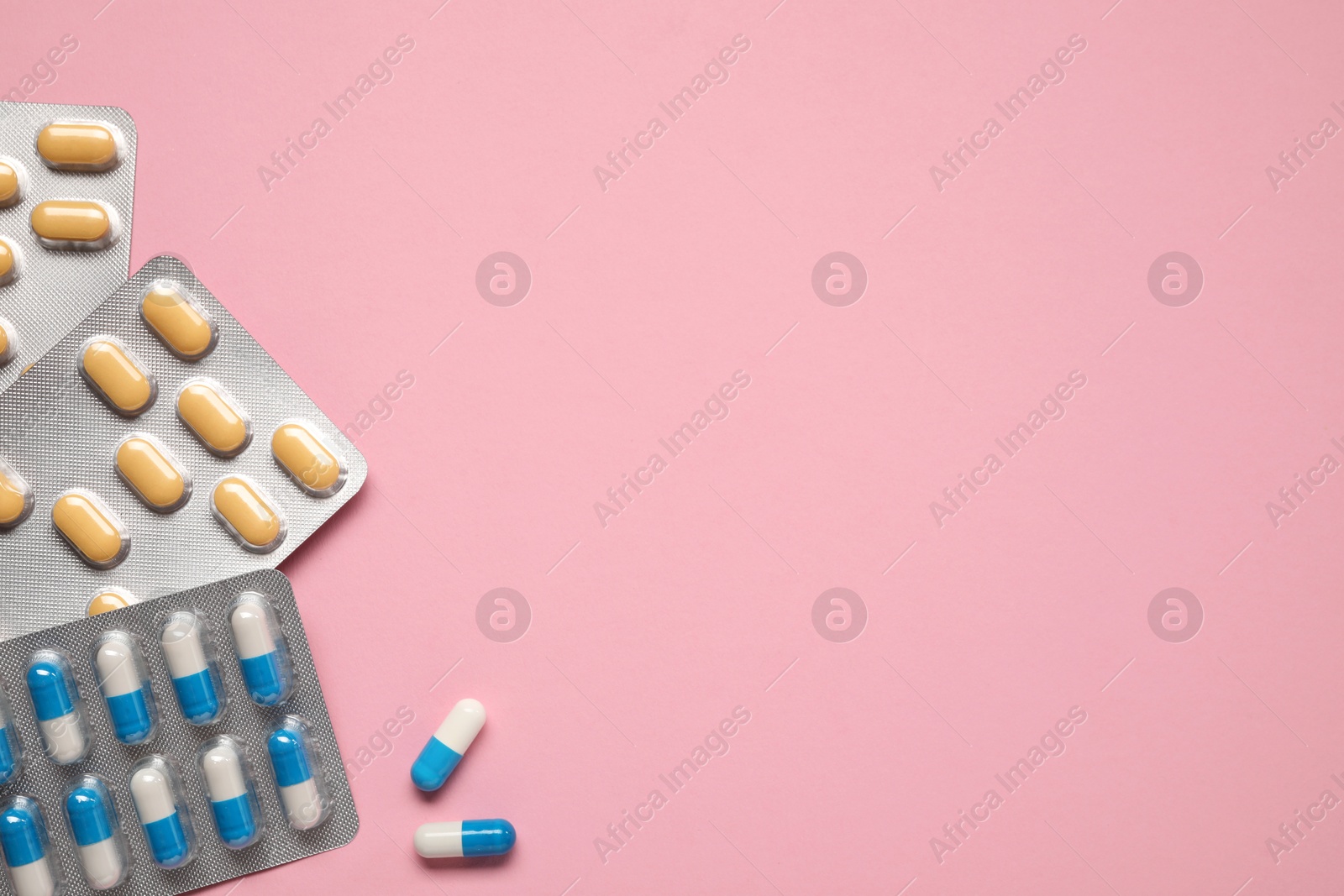 Photo of Different antibiotic pills in blisters on pink background, flat lay. Space for text