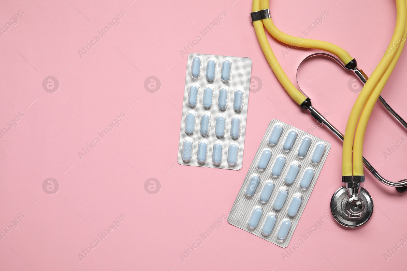 Photo of Antibiotic pills in blisters and stethoscope on pink background, flat lay. Space for text