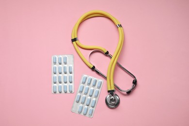 Photo of Antibiotic pills in blisters and stethoscope on pink background, flat lay