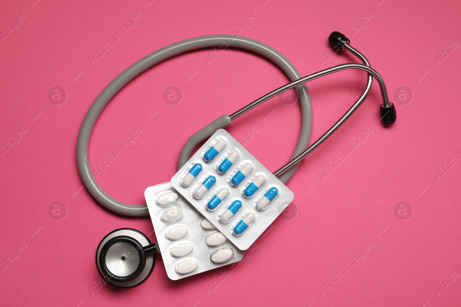 Photo of Different antibiotic pills in blisters and stethoscope on pink background, flat lay