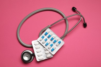 Photo of Different antibiotic pills in blisters and stethoscope on pink background, flat lay