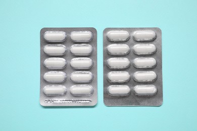 Photo of Antibiotic pills in blisters on light blue background, flat lay