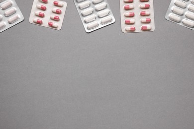 Different antibiotic pills in blisters on gray background, flat lay. Space for text