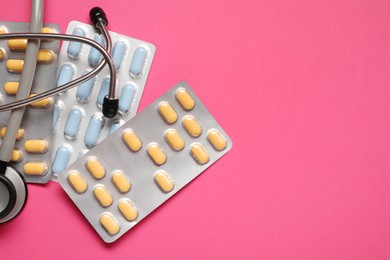 Photo of Different antibiotic pills in blisters and stethoscope on pink background, flat lay. Space for text