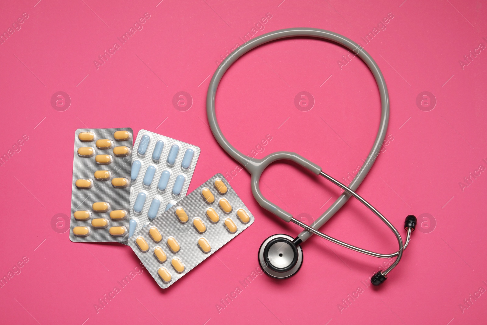 Photo of Different antibiotic pills in blisters and stethoscope on pink background, flat lay