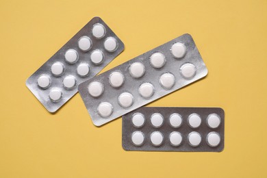 Antibiotic pills in blisters on yellow background, flat lay