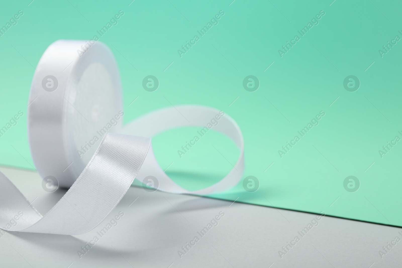 Photo of Beautiful white ribbon reel on color background, closeup. Space for text