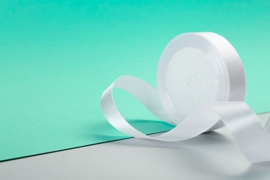 Photo of Beautiful white ribbon reel on color background, closeup. Space for text