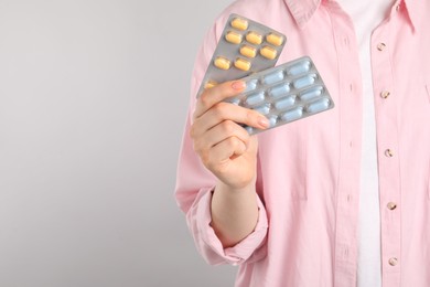 Photo of Woman holding blisters with antibiotic pills on light grey background, closeup. Space for text