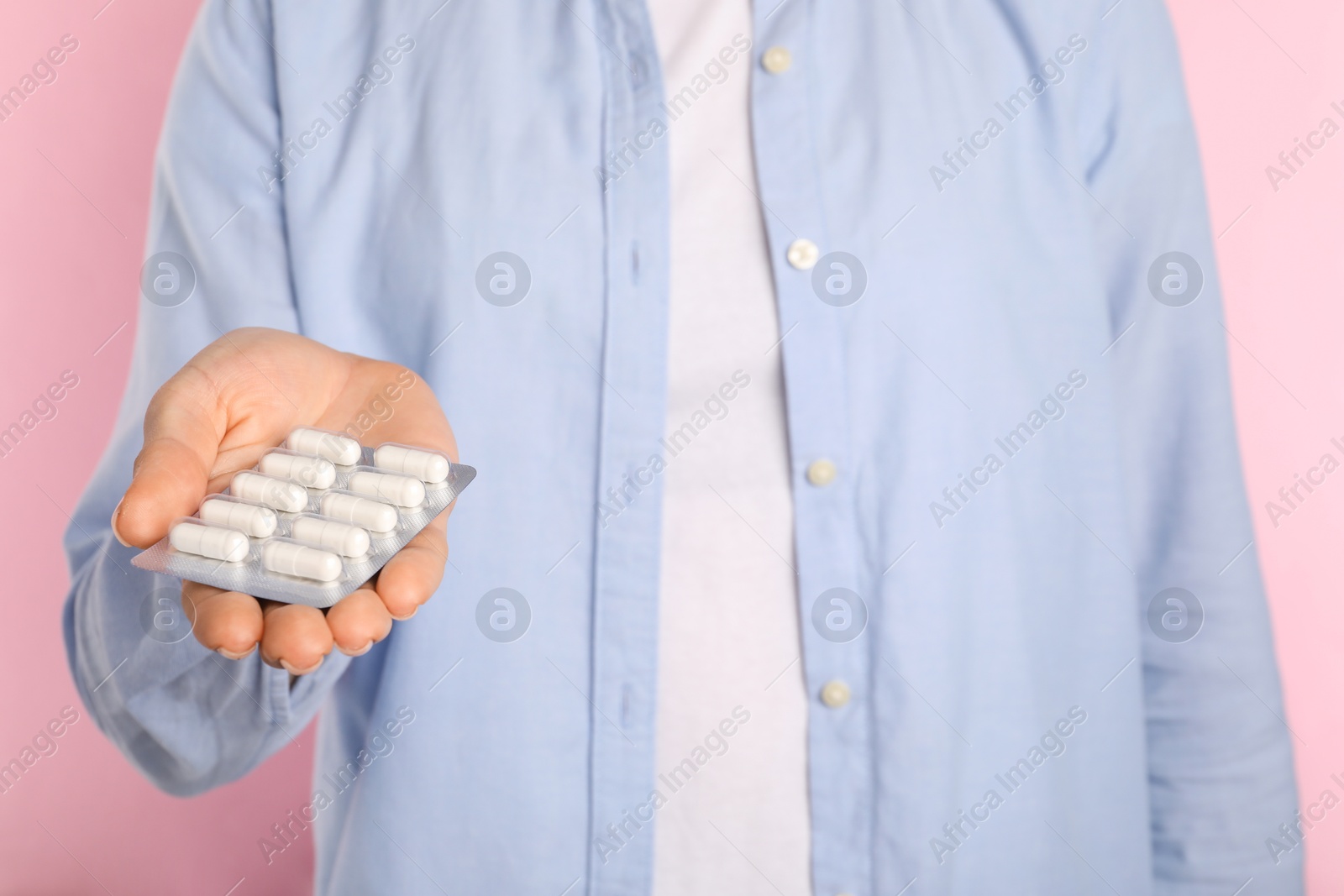 Photo of Woman holding blister with antibiotic pills on pink background, closeup