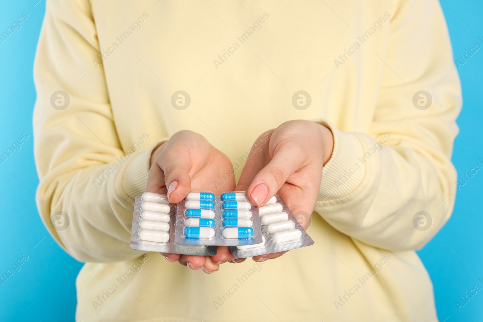 Photo of Woman holding blisters with antibiotic pills on light blue background, closeup