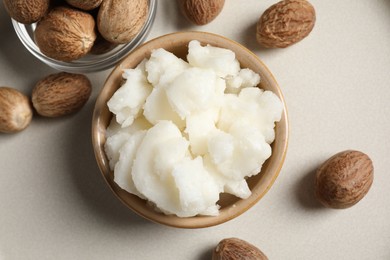 Photo of Shea butter in bowl and nuts on beige table, flat lay