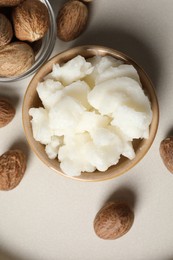 Photo of Shea butter in bowl and nuts on beige table, flat lay