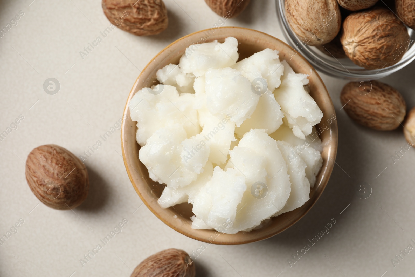 Photo of Shea butter in bowl and nuts on beige table, flat lay