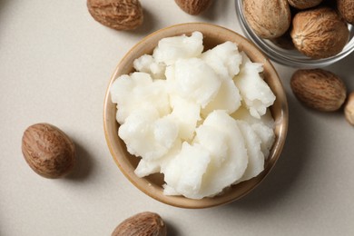 Shea butter in bowl and nuts on beige table, flat lay