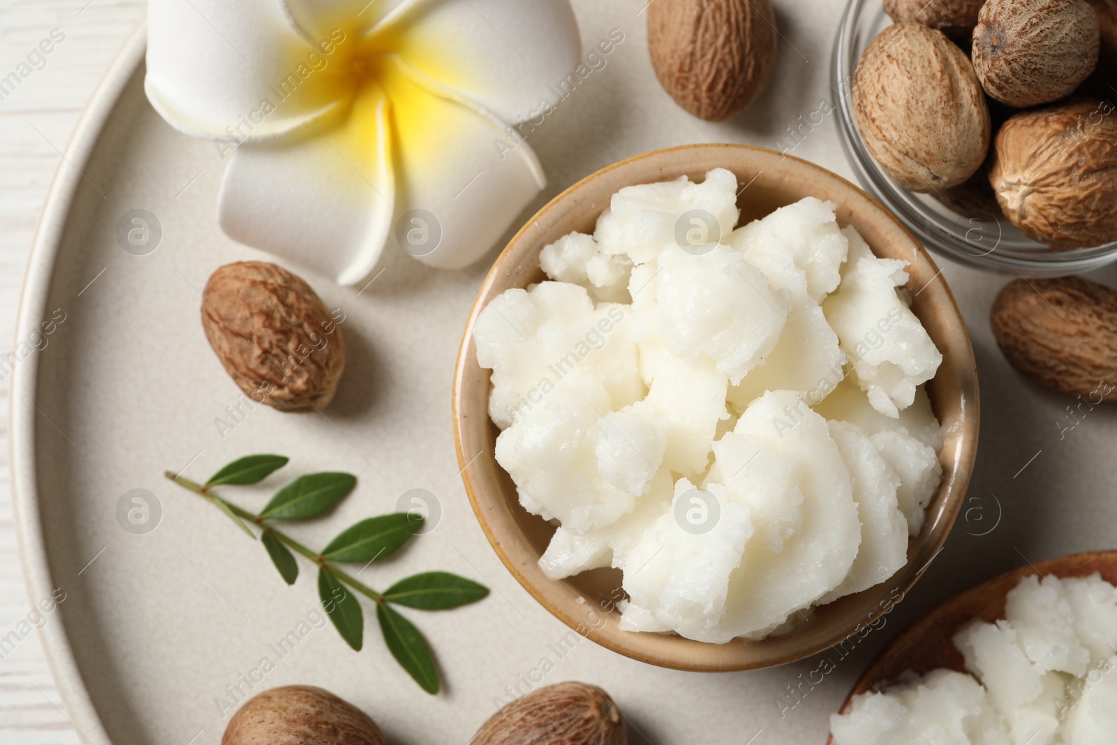 Photo of Shea butter in bowl, flower and nuts on white wooden table, top view