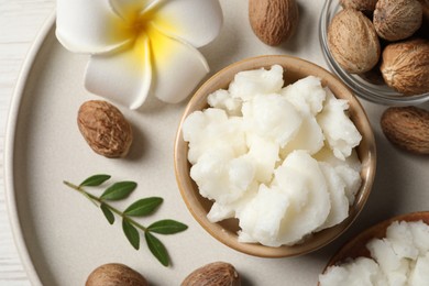 Shea butter in bowl, flower and nuts on white wooden table, top view