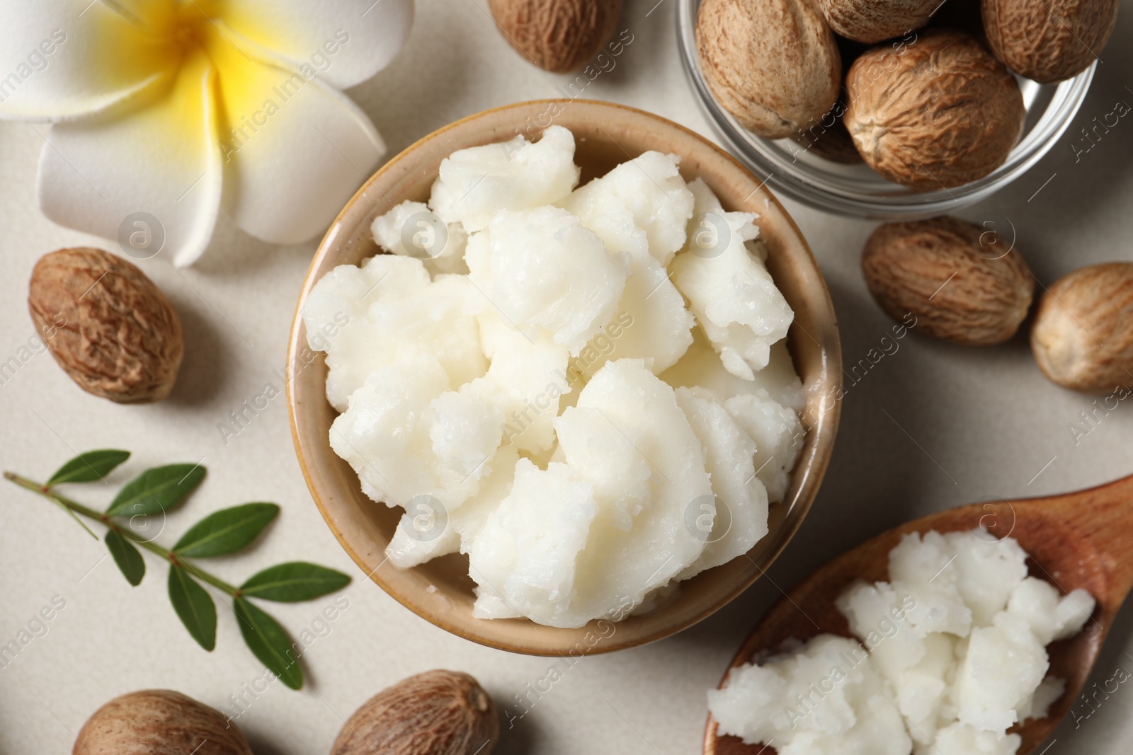 Photo of Shea butter in bowl, flower and nuts on beige table, flat lay