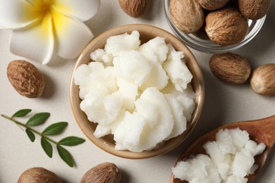 Photo of Shea butter in bowl, flower and nuts on beige table, flat lay