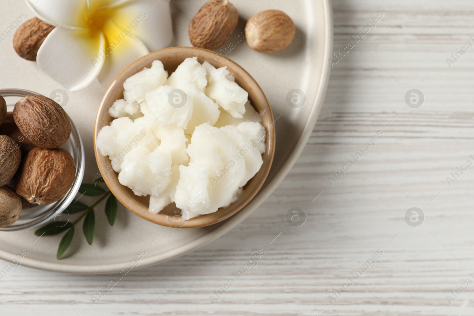 Photo of Shea butter in bowl, flower and nuts on white wooden table, top view. Space for text