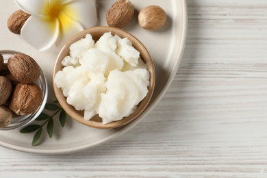 Shea butter in bowl, flower and nuts on white wooden table, top view. Space for text