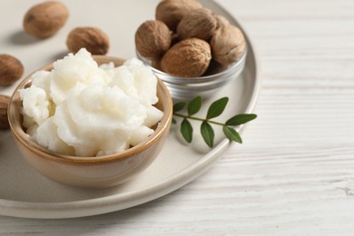 Shea butter in bowl and nuts on white wooden table, space for text