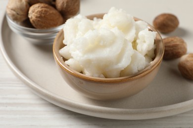 Photo of Shea butter in bowl and nuts on white wooden table, closeup