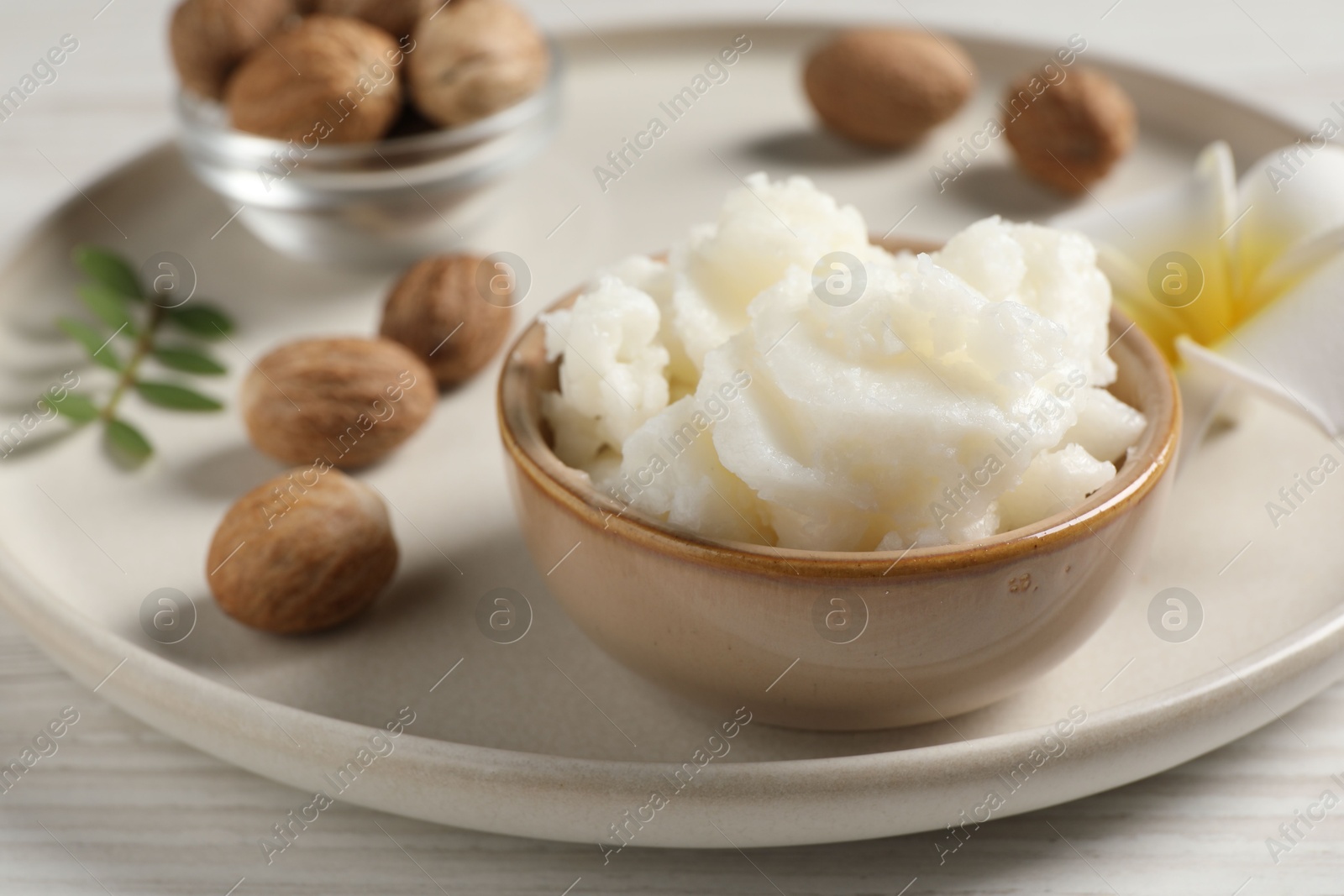 Photo of Shea butter in bowl, flower and nuts on white wooden table, closeup