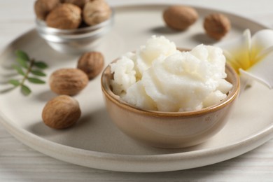 Shea butter in bowl, flower and nuts on white wooden table, closeup