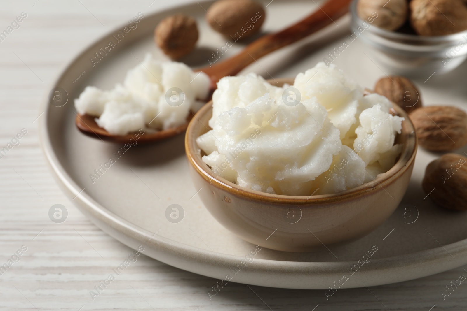 Photo of Shea butter in bowl and nuts on white wooden table, closeup