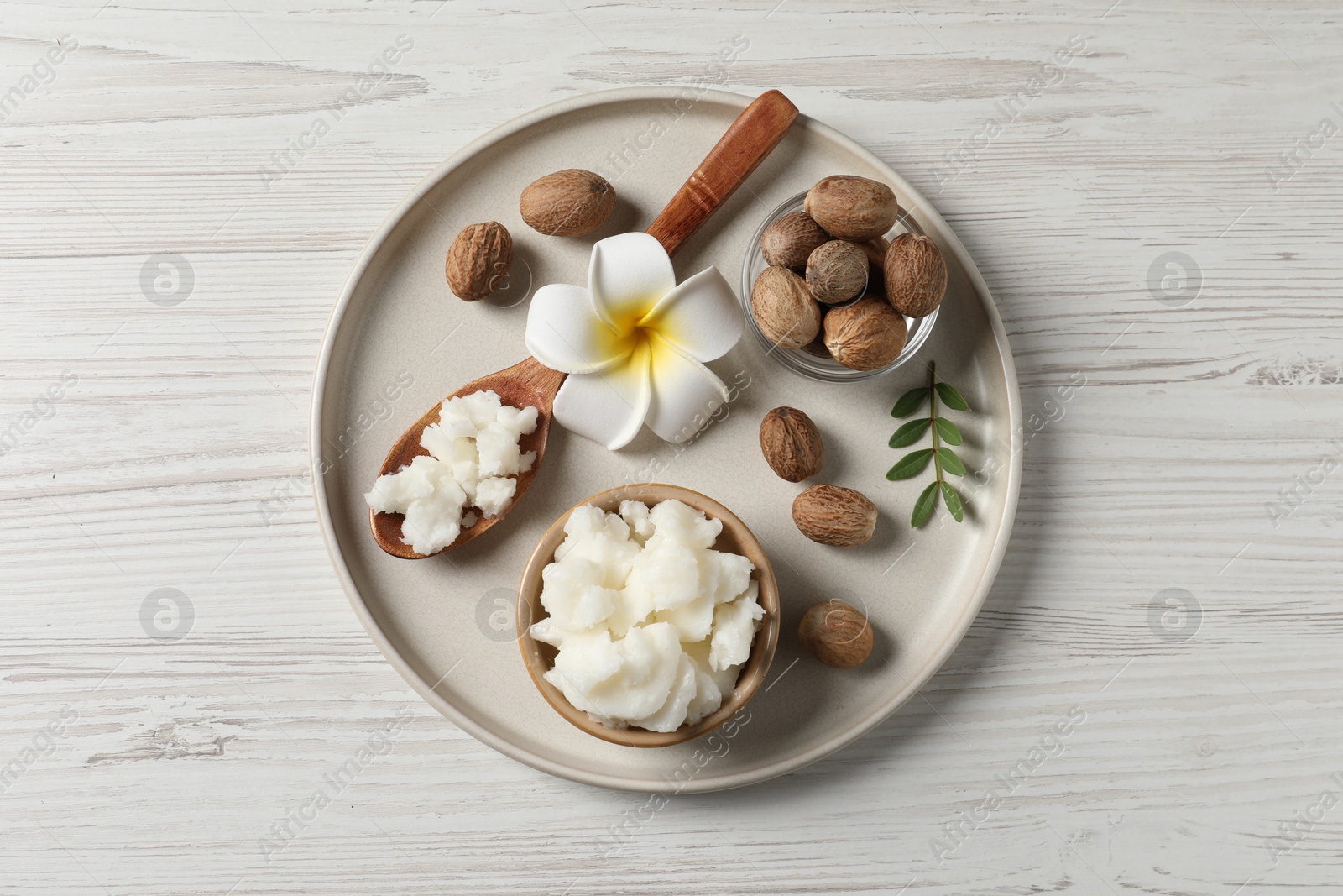 Photo of Shea butter in bowl, flower and nuts on white wooden table, top view