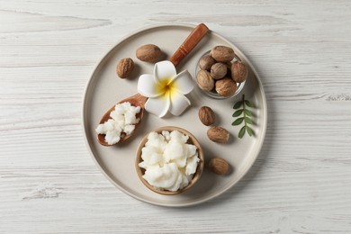 Shea butter in bowl, flower and nuts on white wooden table, top view