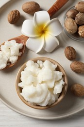 Photo of Shea butter in bowl, flower and nuts on white wooden table, top view