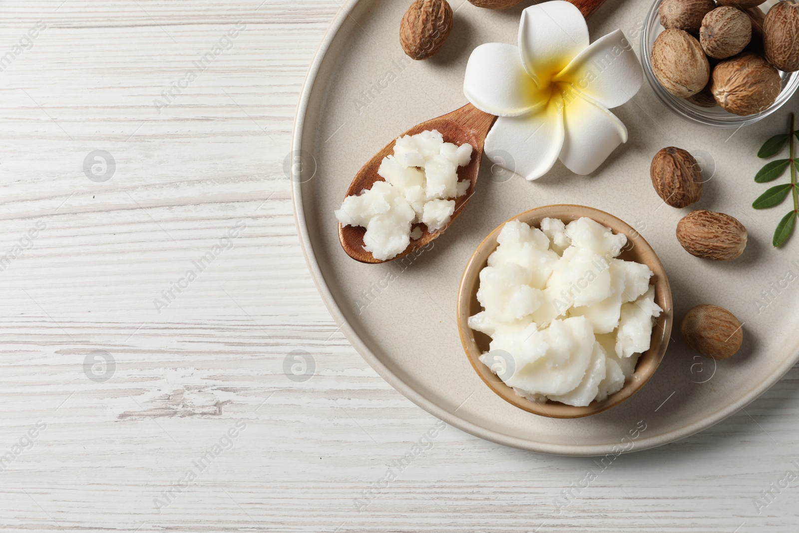 Photo of Shea butter in bowl, flower and nuts on white wooden table, top view. Space for text