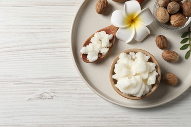 Shea butter in bowl, flower and nuts on white wooden table, top view. Space for text