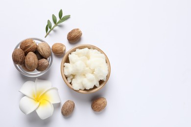 Photo of Shea butter in bowl, flower and nuts on white background, flat lay. Space for text