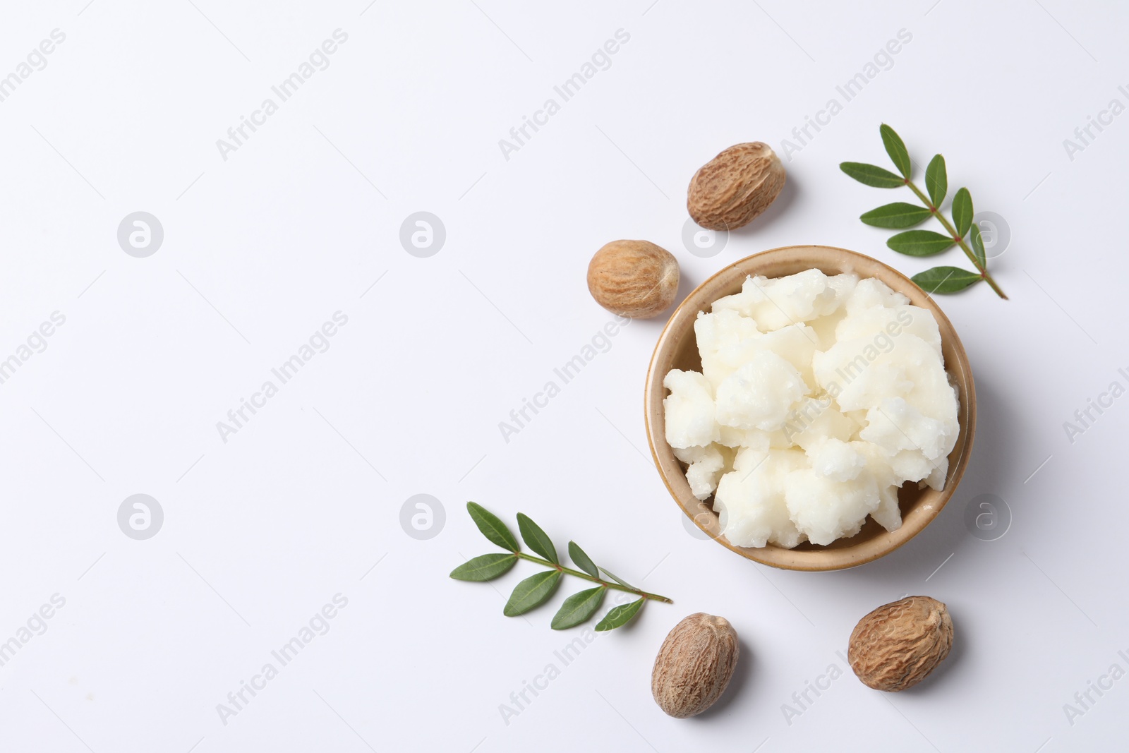 Photo of Shea butter in bowl and nuts on white background, flat lay. Space for text