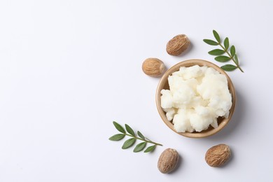 Shea butter in bowl and nuts on white background, flat lay. Space for text