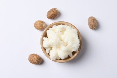 Shea butter in bowl and nuts on white background, flat lay