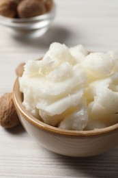 Photo of Shea butter in bowl and nuts on white wooden table, closeup