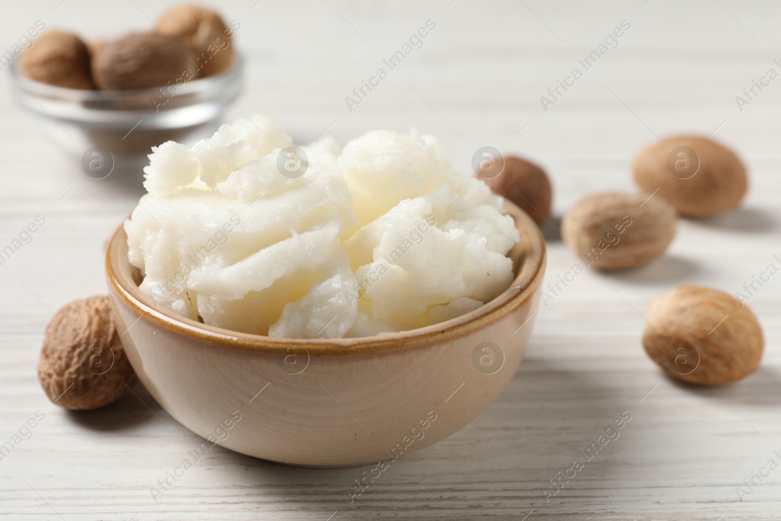 Photo of Shea butter in bowl and nuts on white wooden table, closeup