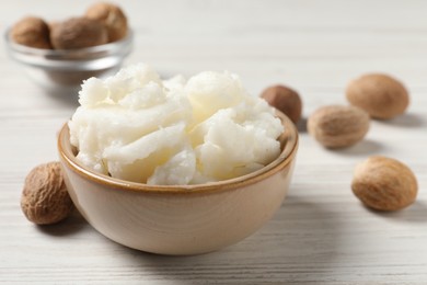 Shea butter in bowl and nuts on white wooden table, closeup